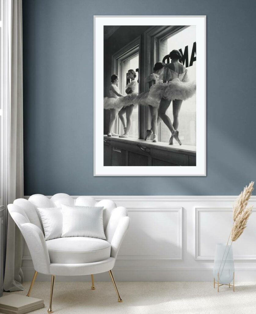 Framed black and white Alfred Eisenstaedt Ballerinas in the Window hanging on a grey wall above a white one seater