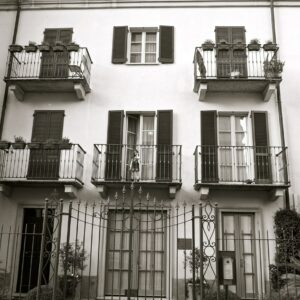 Black and white photo of a building with a little girl standing on a second floor balcony looking at the photographer