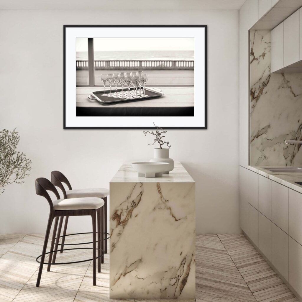 Black and white framed picture off a tray of filled champagne glasses on a table. The picture hangs on a wall in a kitchen 