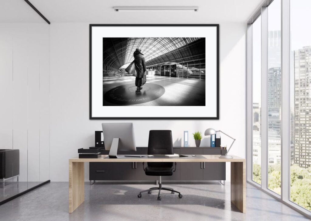 Framed black and white photo of the statue of Sir John Betjeman at the St Pancreas station. The picture is hanging on a wall behind an office desk.