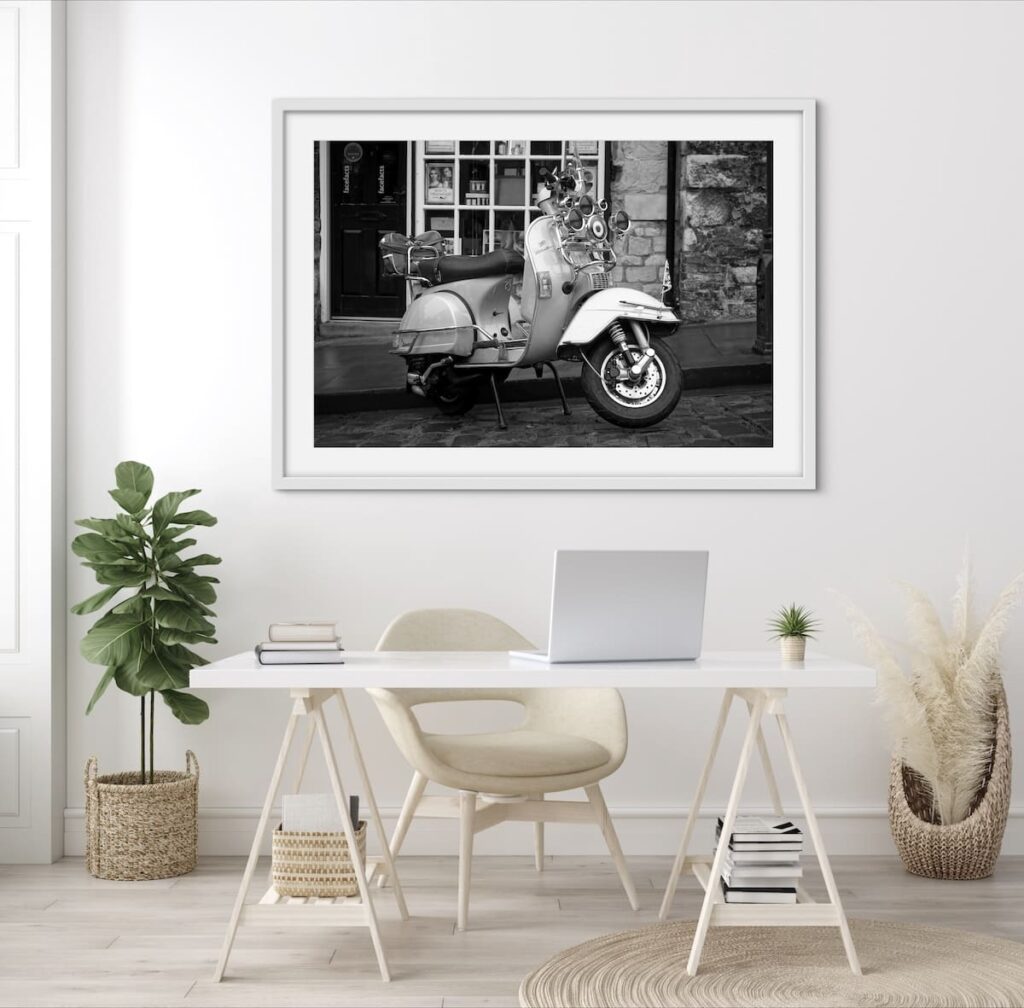 Framed black & white photo of a Vespa on a wall behind a desk.