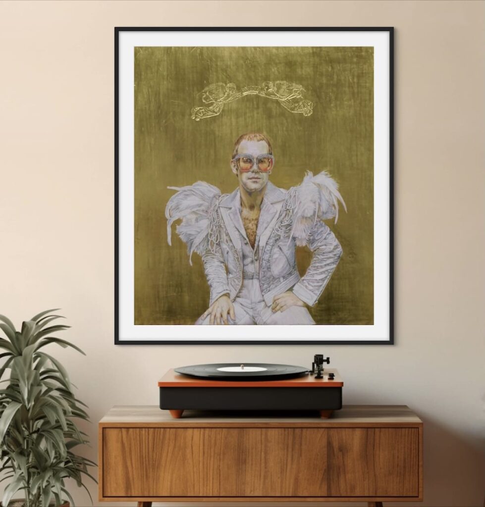 thing! Here’s the alt text for this image: Alt text: A framed artwork hanging on a wall above a wooden console table with a record player on top. The artwork features a person dressed in an elaborate, feathered costume with a gold background. The person is seated with hands resting on their knees. There is a decorative element above the person's head in the artwork. A potted plant is placed to the left of the console table. The setting appears to be a stylish and well-decorated room, possibly a living room or a music room.
