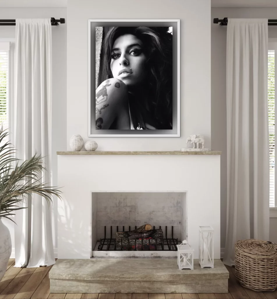 Modern living room with a white fireplace and neutral décor, featuring a large framed black-and-white portrait of a woman with dark hair and visible shoulder tattoos mounted above the mantel as a bold focal point.
