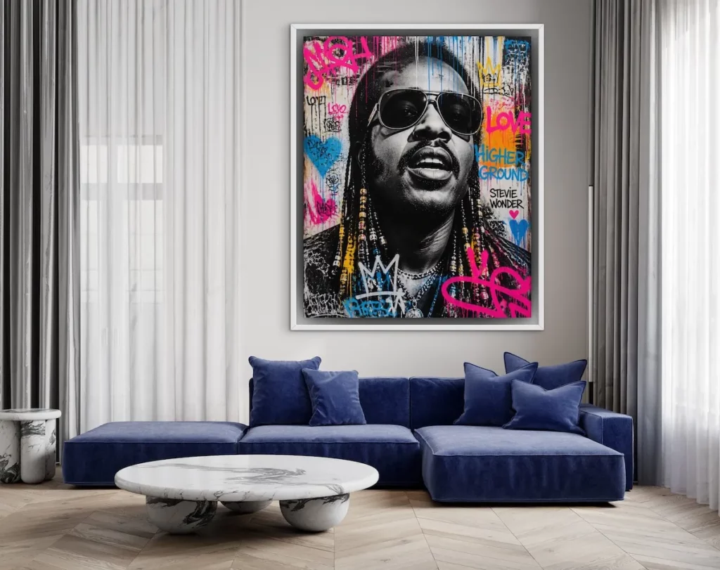 Contemporary living room with a deep blue sectional sofa and round marble coffee table, featuring a large framed pop art portrait of a man wearing sunglasses. The colorful artwork combines graffiti-inspired text, hearts, crowns, and bold brushstrokes in pink, blue, yellow, and orange, creating a vibrant focal point against the neutral interior.
