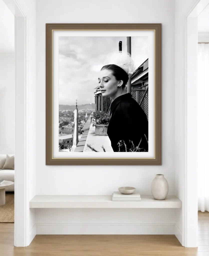 This image shows a framed black and white photograph of Audrey Hepburn looking out over a city from a balcony.