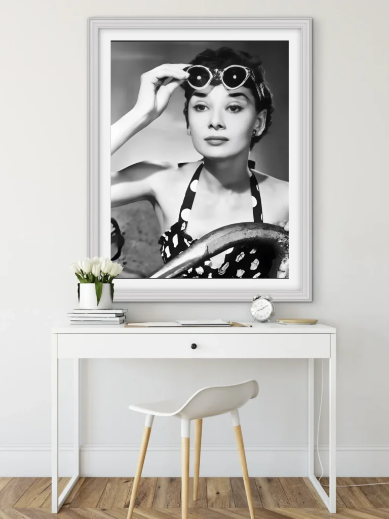 A black and white framed photograph of Audrey Hepburn wearing sunglasses and a polka dot dress, displayed above a white desk and chair