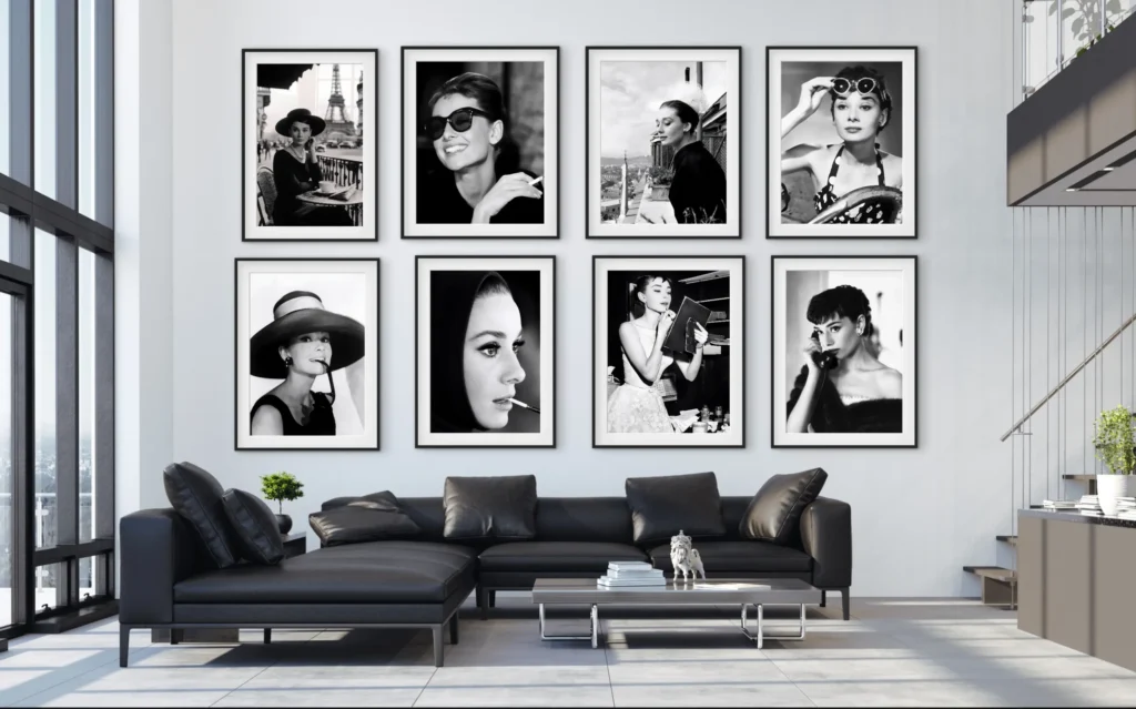 A gallery wall featuring eight framed black-and-white portraits of Audrey Hepburn displayed above a modern black leather sectional sofa in a well-lit living room.