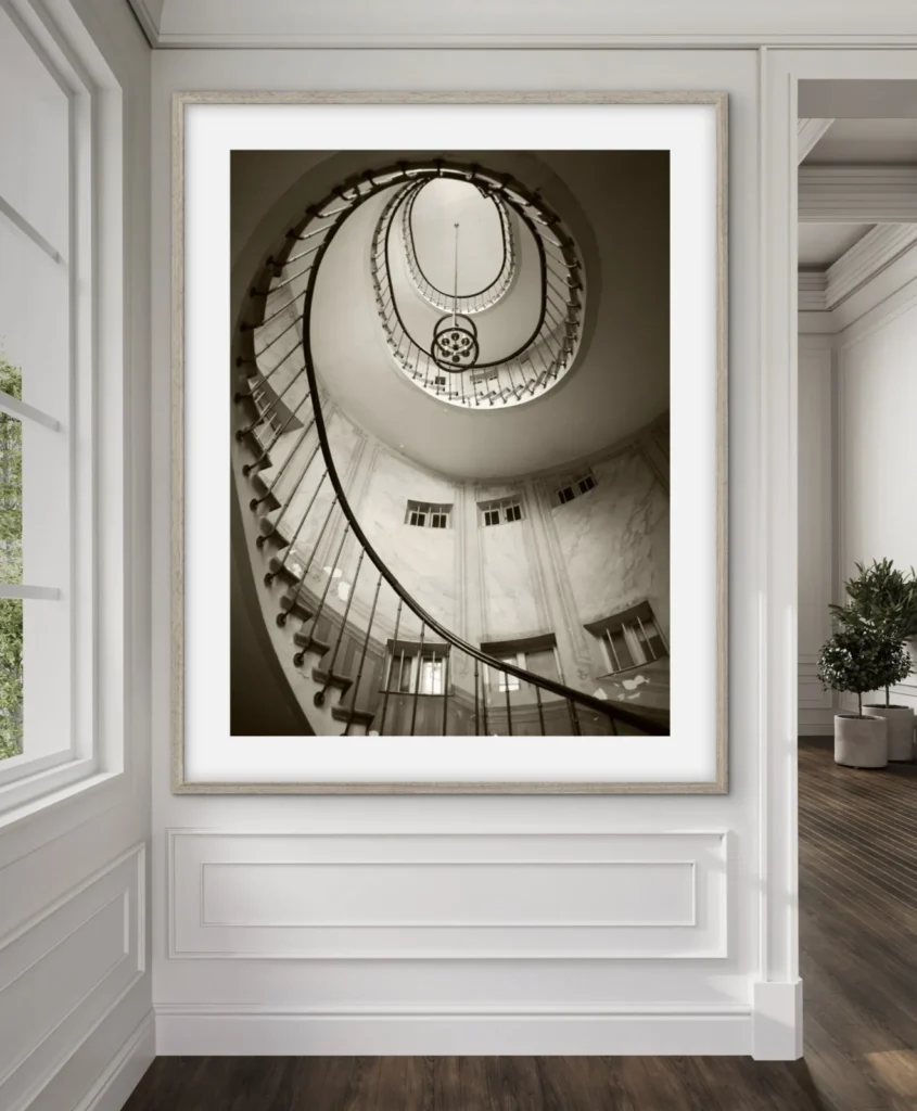 A black and white photograph looking up at a spiral staircase inside a building with a light fixture hanging in the center.