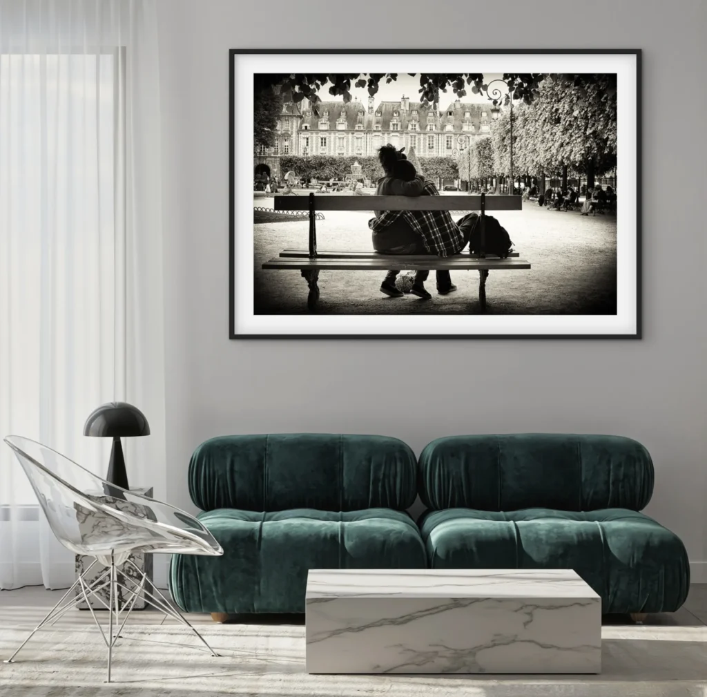 a black and white photograph of a couple sitting on a park bench, with a large building and trees in the background. The photograph is displayed above a modern green velvet sofa and a marble coffee table.